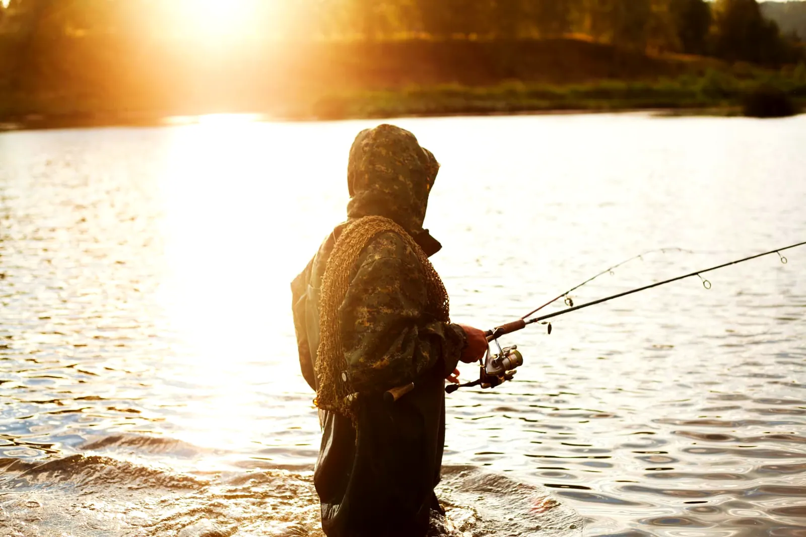 Angler in waders casting a spinning rod in a river at sunset